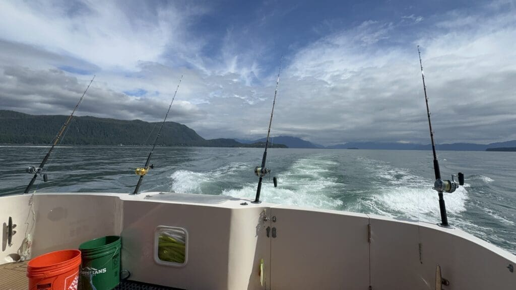 Juneau fishing charter trolling rods on the aft deck of the M/Y Sir Reel with Southeast Alaska mountains in the background