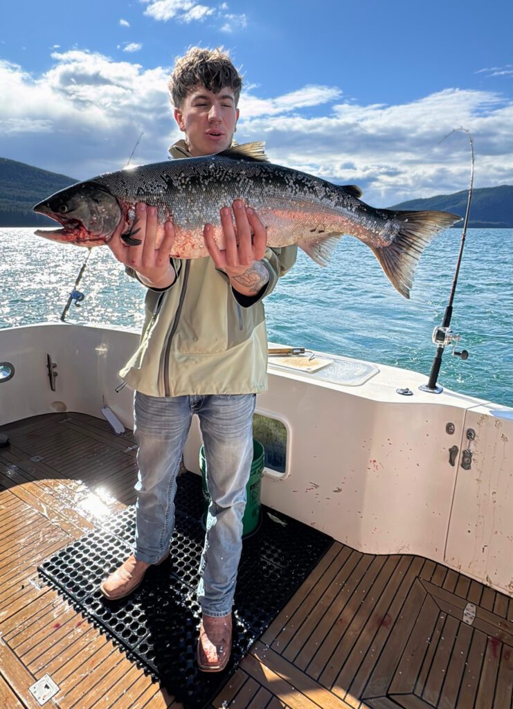 A guest holds up a fresh salmon caught while charter fishing in Alaska with Adventure Fishing Tours in Juneau