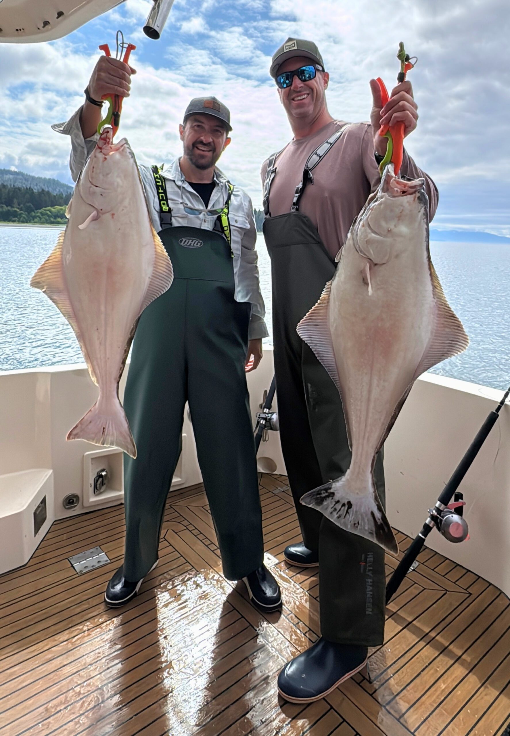 Anglers on a fishing charter in Alaska holding two halibut mountains behind them
