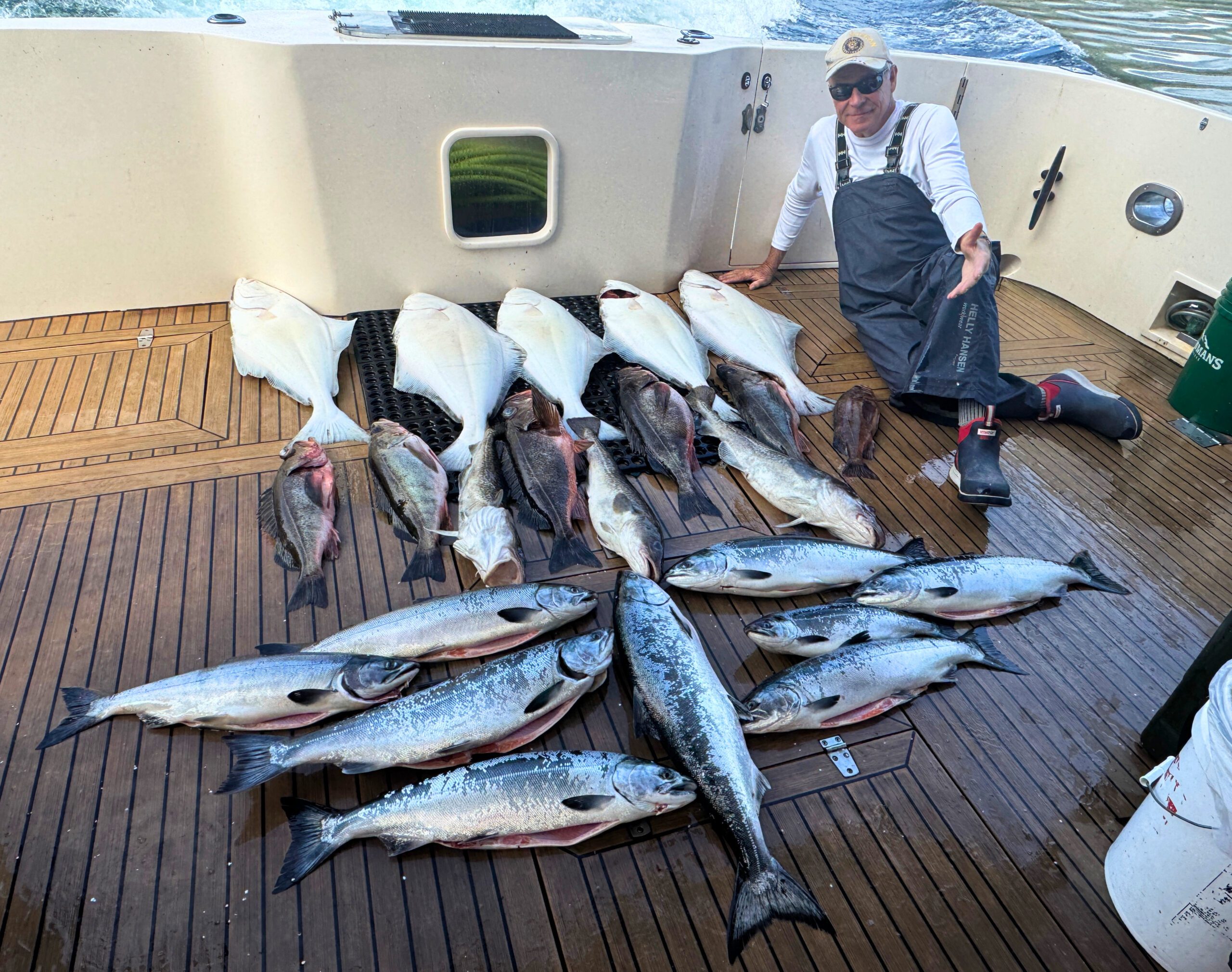 Crew member kneeling beside a mixed catch of salmon and halibut on the deck of a Juneau fishing charter