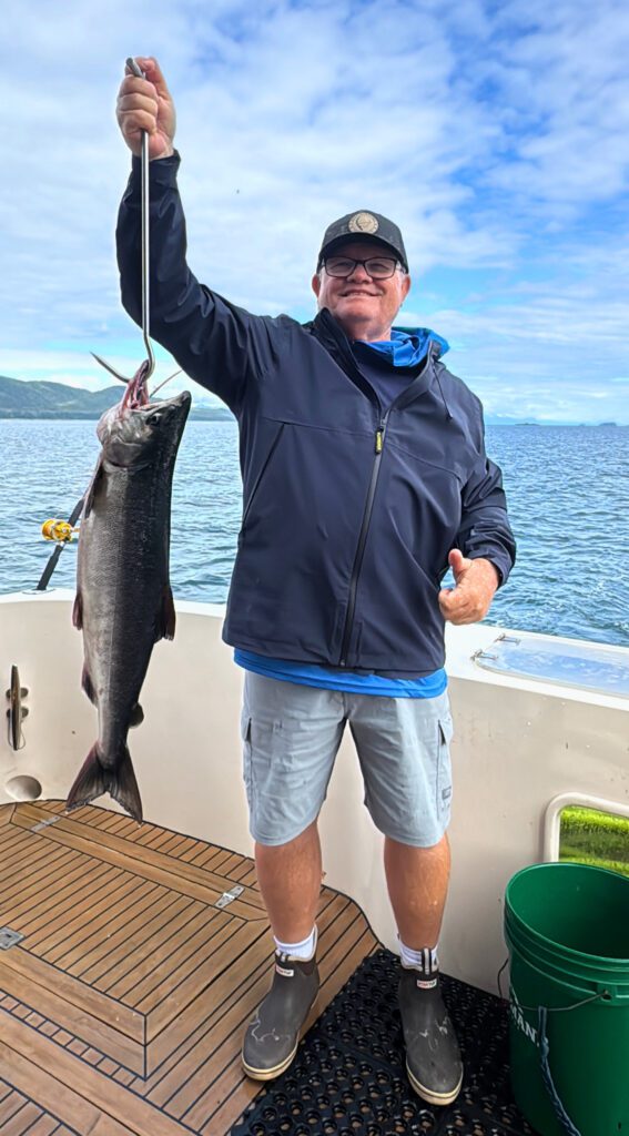 Angler proudly holding a bright salmon on the deck of a charter boat near Juneau, with Southeast Alaska mountains in the background